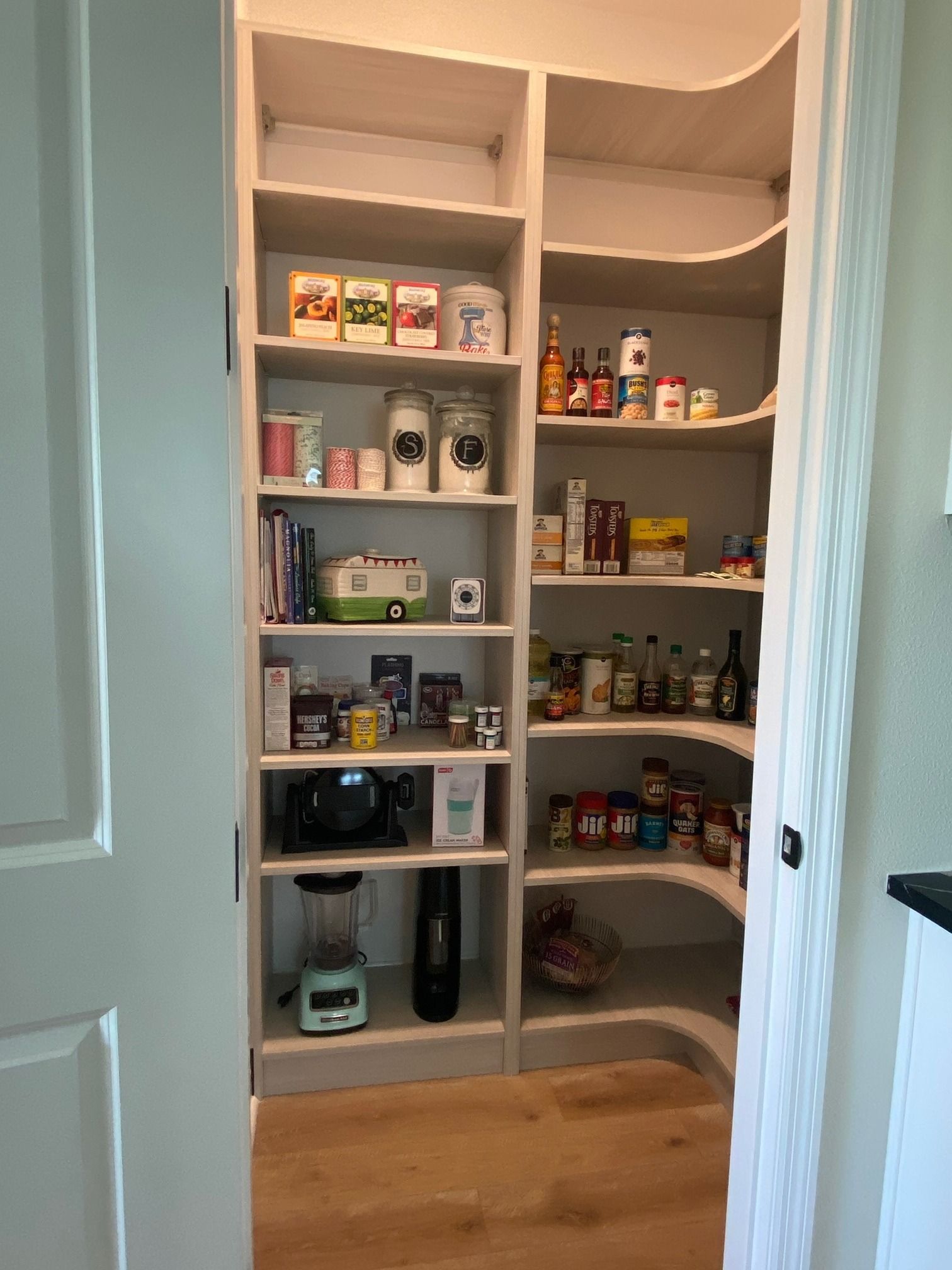 Open pantry closet with shelves stocked with groceries and kitchen items