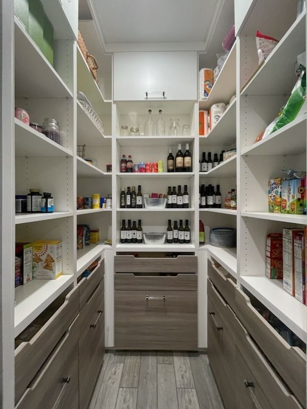 Neat walk-in pantry with white shelves stocked with jars, cans, and bottles, and a wood cabinet center.