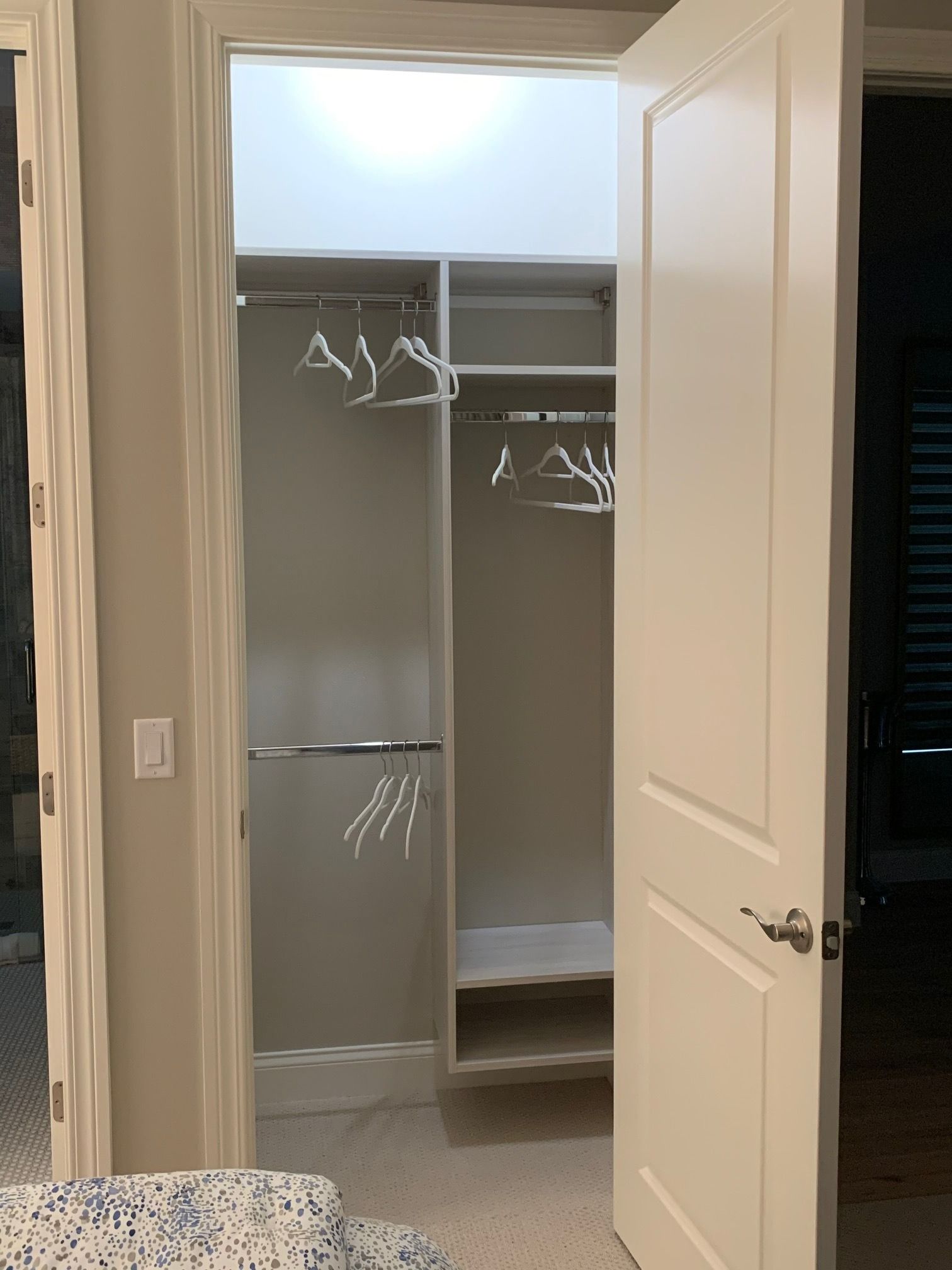 Open closet with white shelves and hanging rods in a doorway, inside a carpeted room.