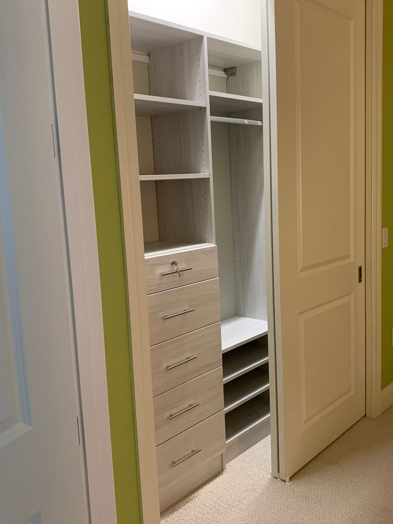 Open closet with white shelves, drawers, hanging rod, and shoe racks in a carpeted hallway