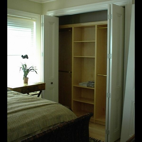Bedroom with open built-in closet, bed at left, and window with potted plant.