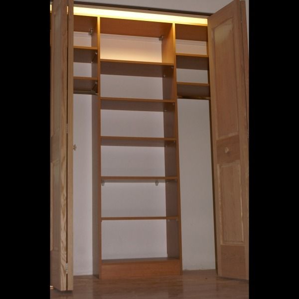 Open wooden closet with built-in shelves and drawers, illuminated by warm overhead light.