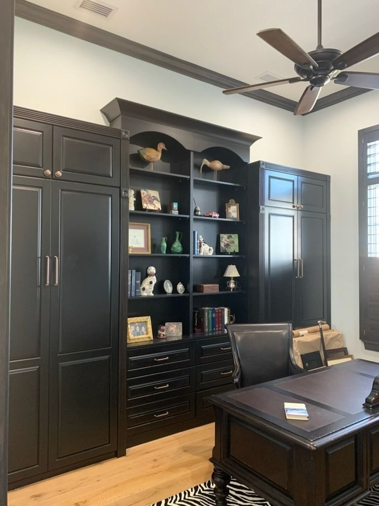 Home office with dark built-in cabinets, open shelves, and a wooden desk under a ceiling fan.