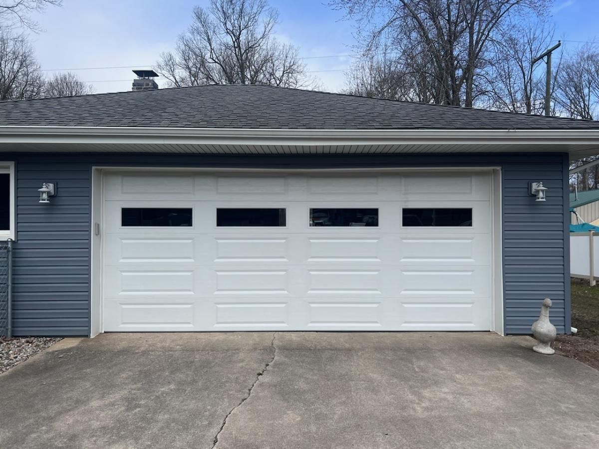 A white garage door is sitting in front of a blue house.