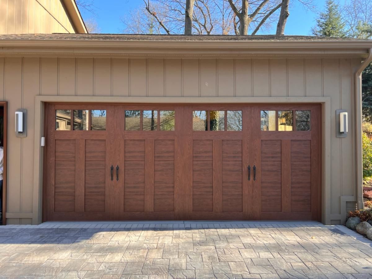 A large wooden garage door with a brick driveway in front of it.