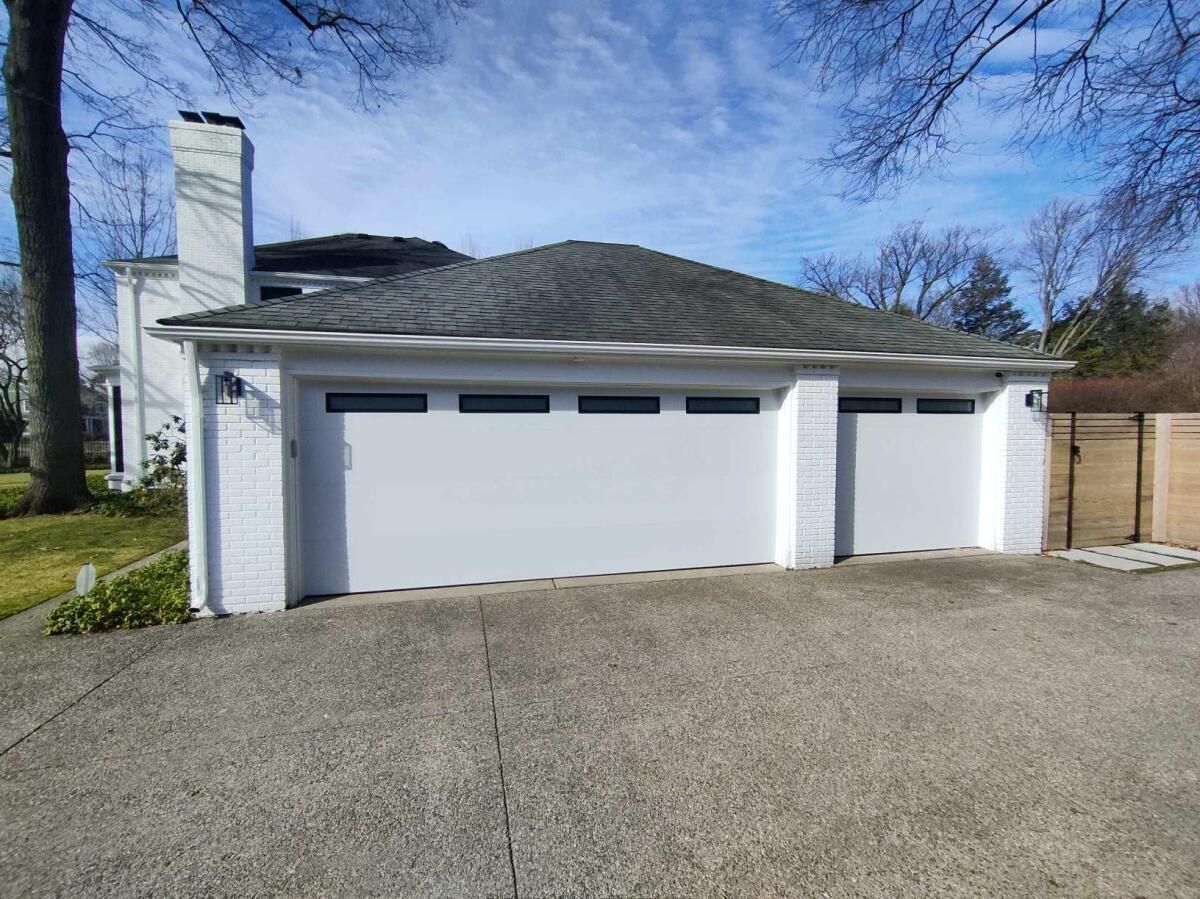 A white garage door is sitting in front of a white house.
