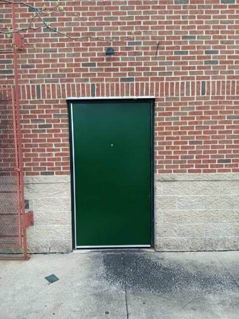 A green door is on the side of a brick building