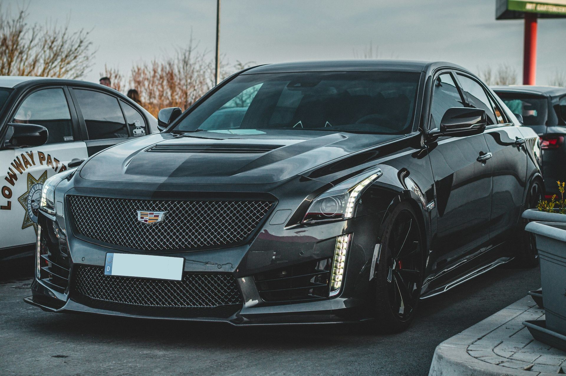 A black cadillac is parked in a parking lot next to a police car.