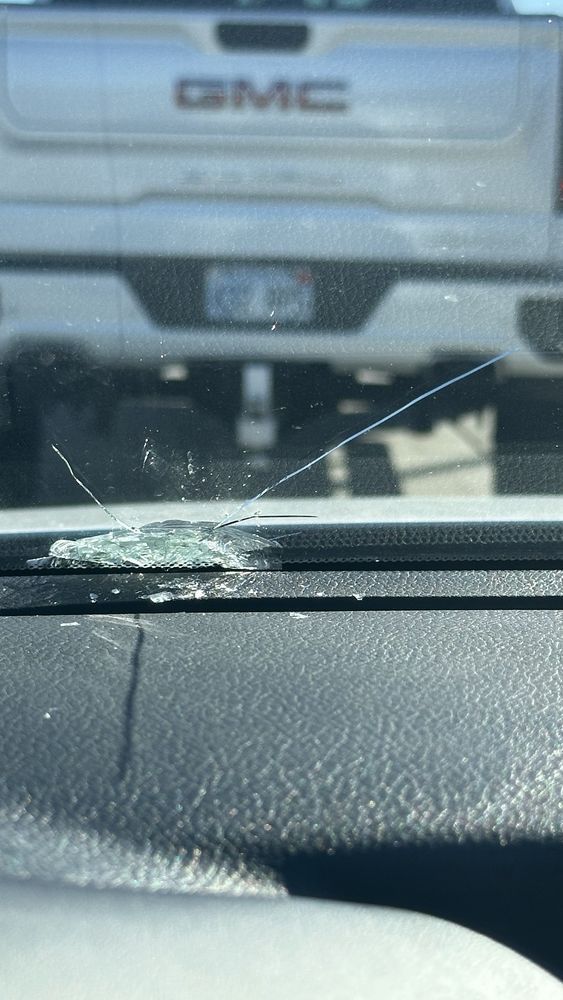 A gmc truck is parked behind a car with a cracked windshield.