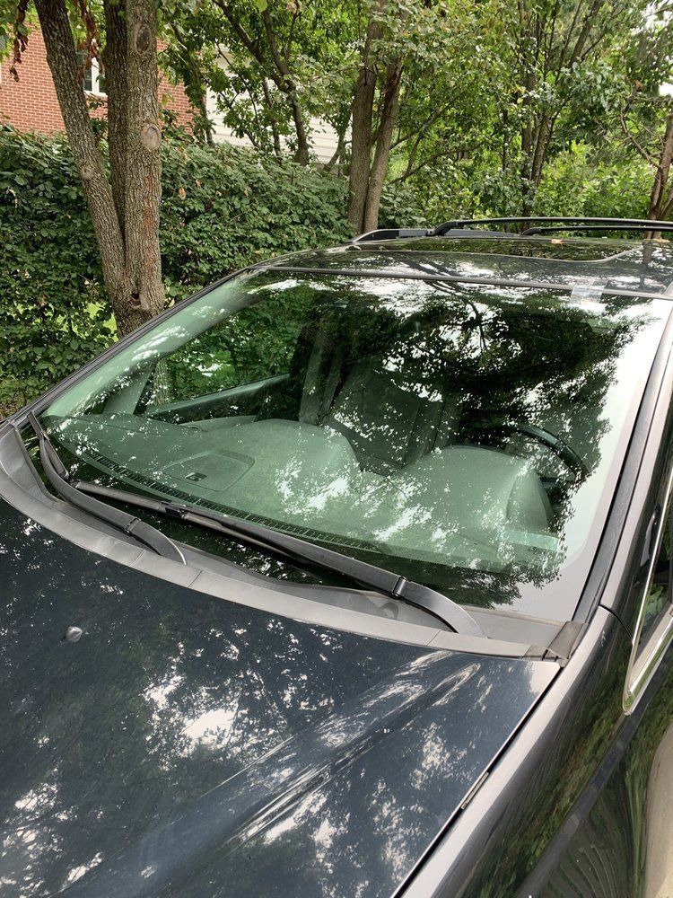 A black suv is parked in a driveway with trees in the background.