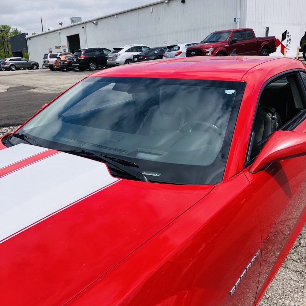 A red car with white stripes on the hood is parked in a parking lot