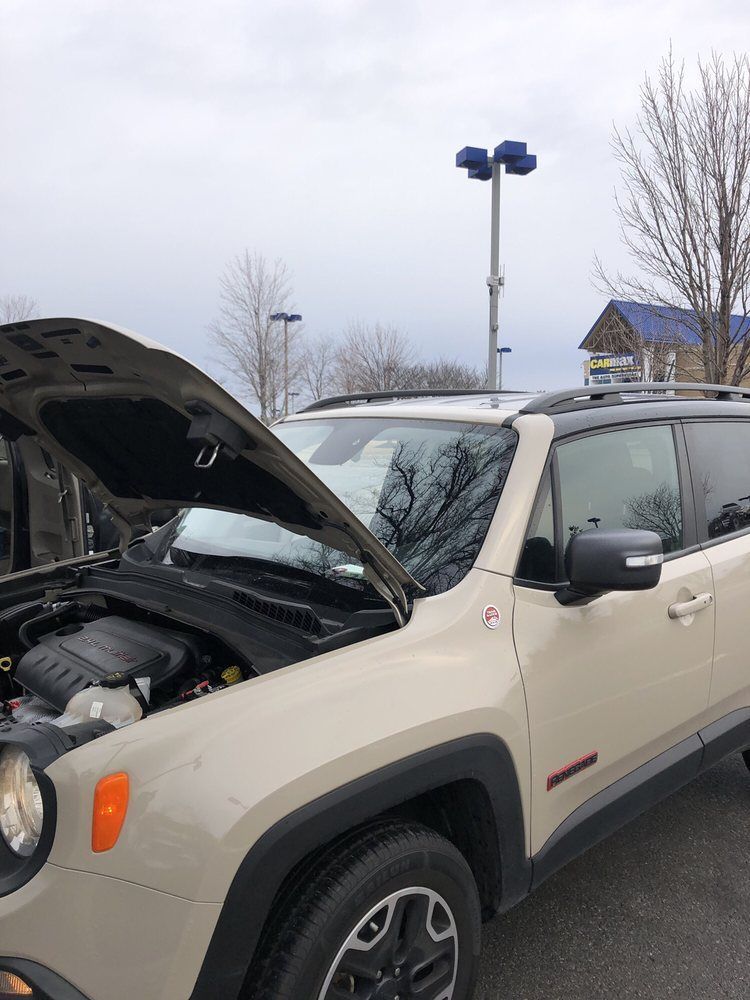 A white jeep renegade with the hood open is parked in a parking lot.