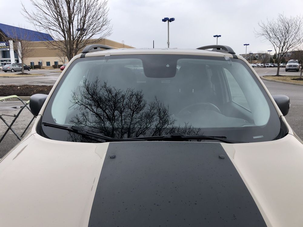 A white car with a black stripe on the hood is parked in a parking lot.