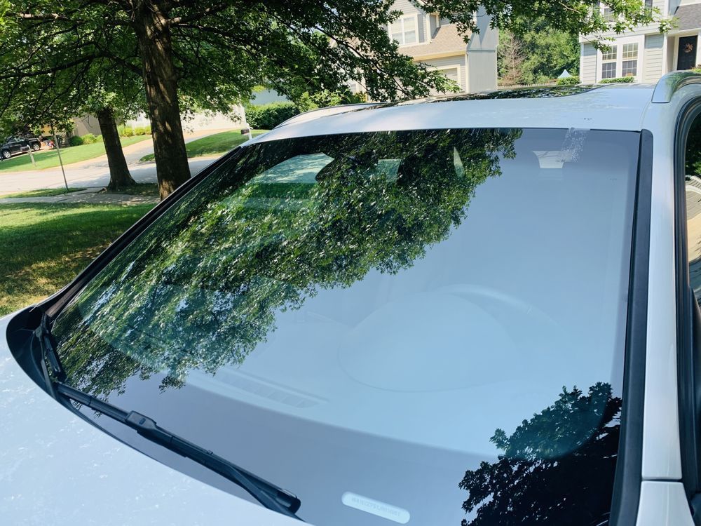 A white car with a reflection of trees in the windshield