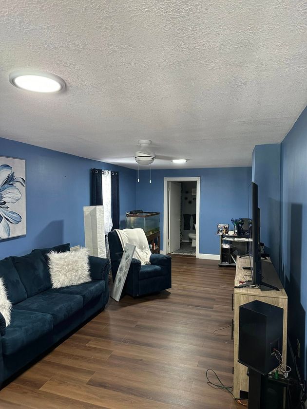 Blue living room with dark sofa, fireplace, hardwood floor, and ceiling fan