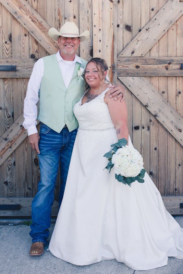 Couple in wedding attire posing in front of rustic wooden barn doors