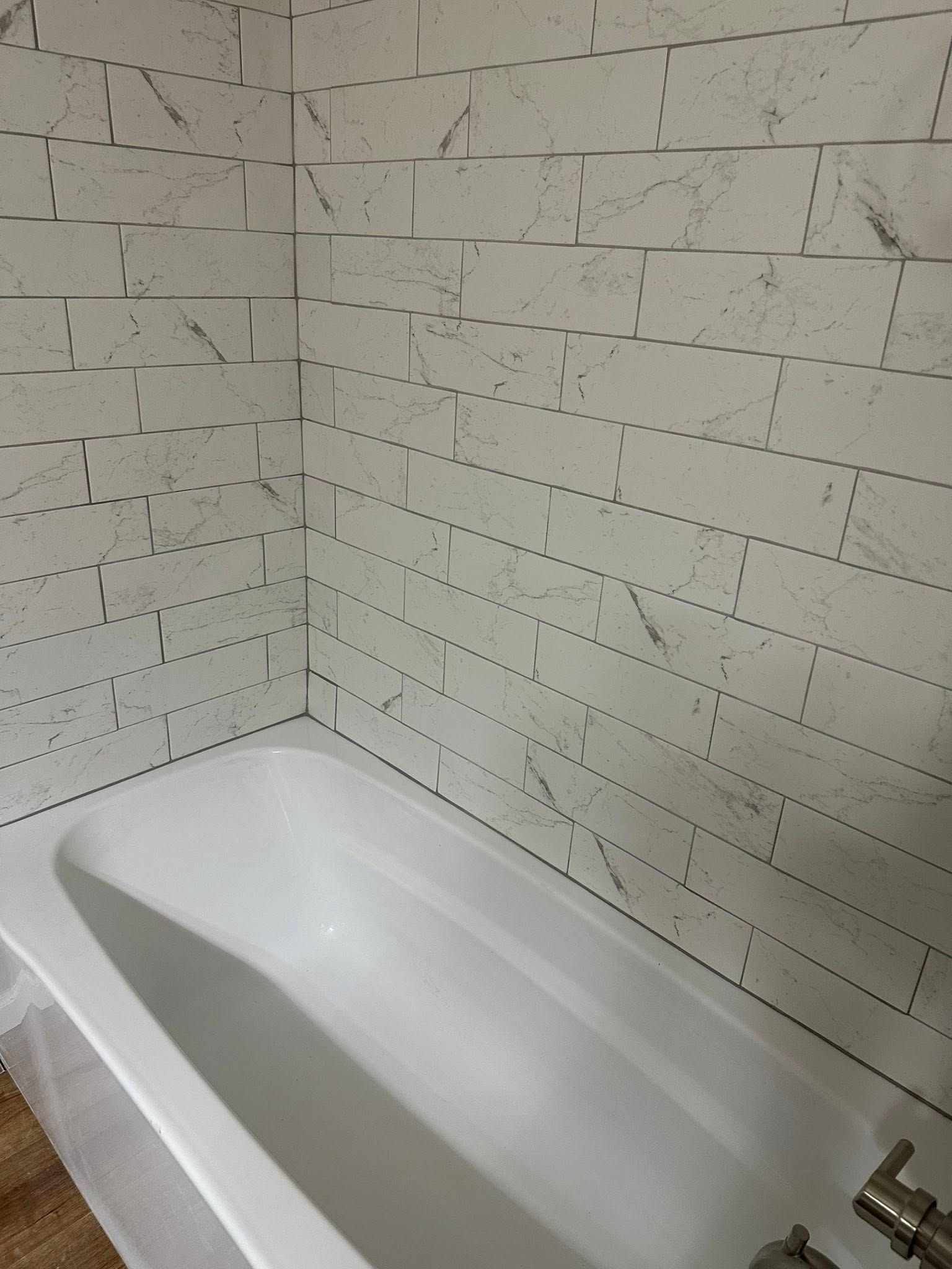 White bathtub in a tiled bathroom corner with a faucet visible on the right