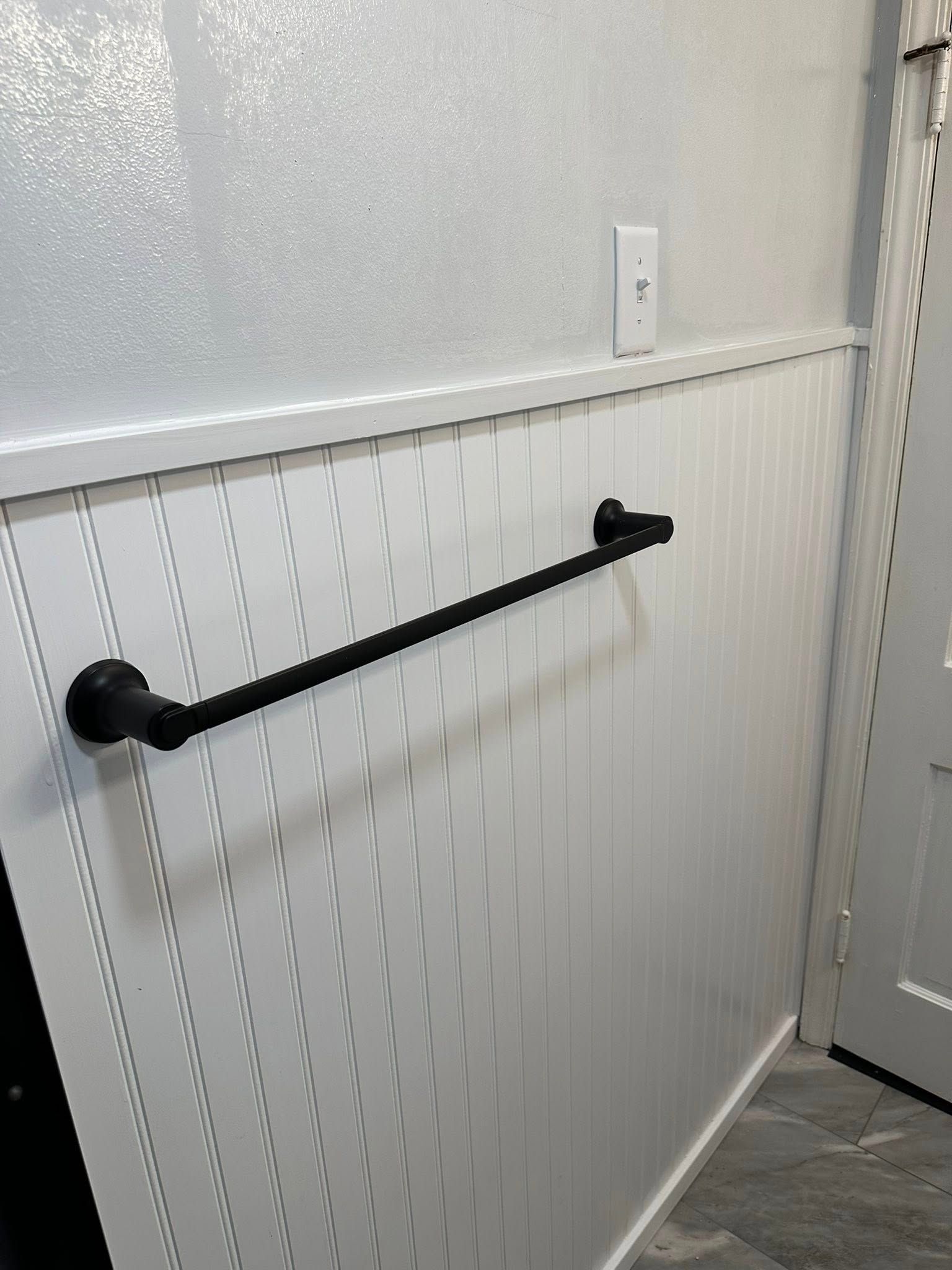 Black wall-mounted handrail on a white wainscoted hallway wall near a door.