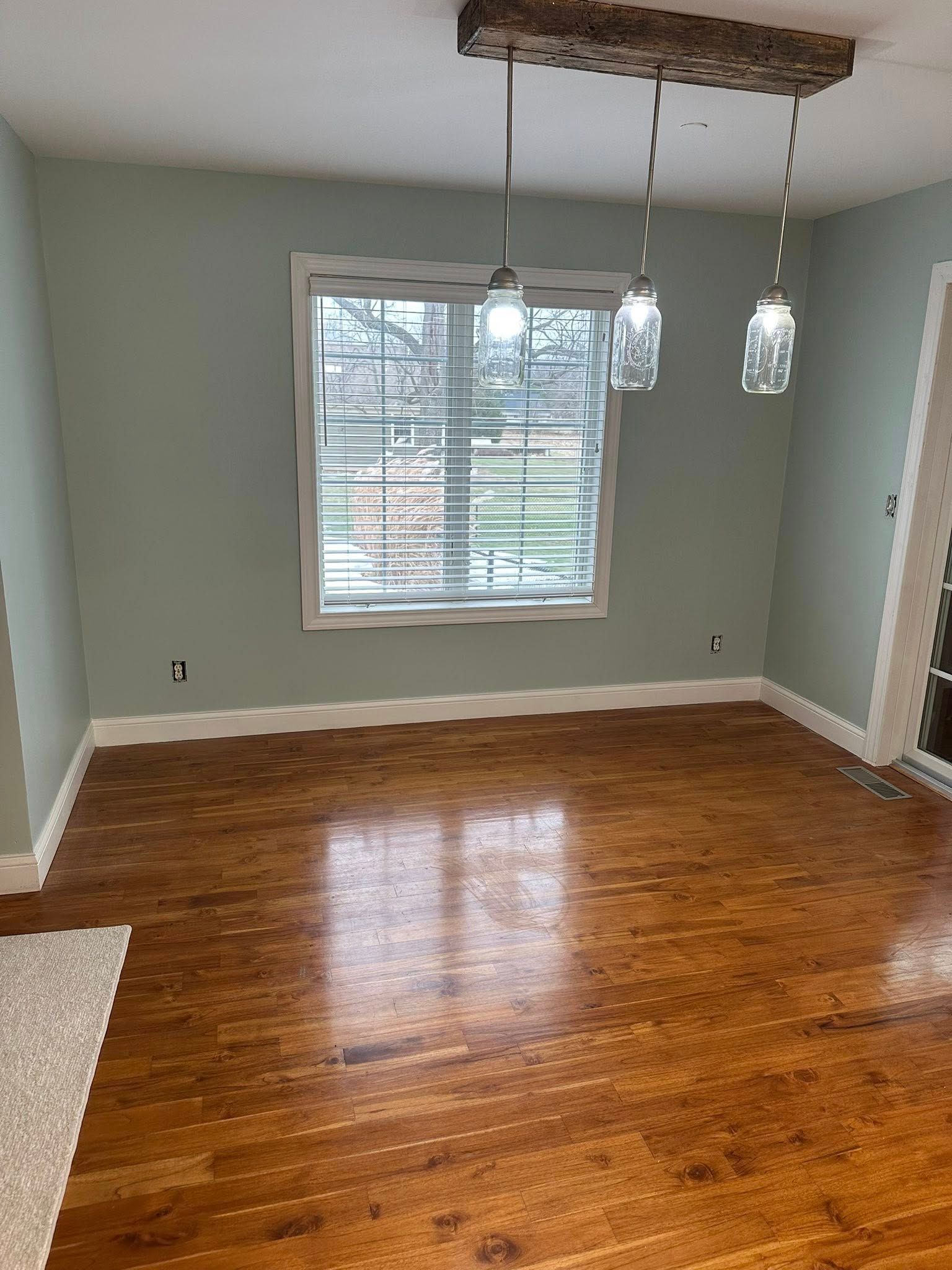Empty room with glossy hardwood floors, gray walls, a window, and three pendant lights over a small ceiling cutout
