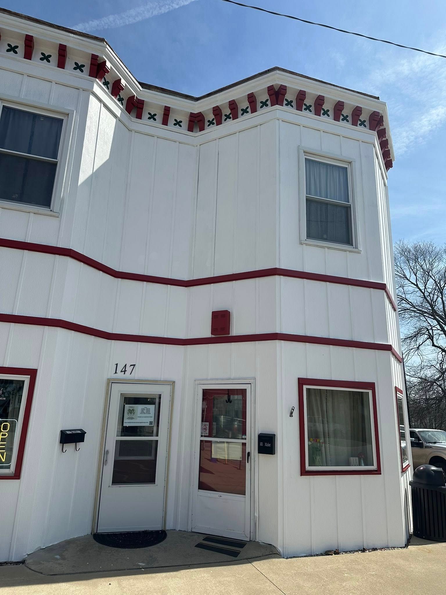 White two-story building with red trim, a storefront door and windows, under a blue sky