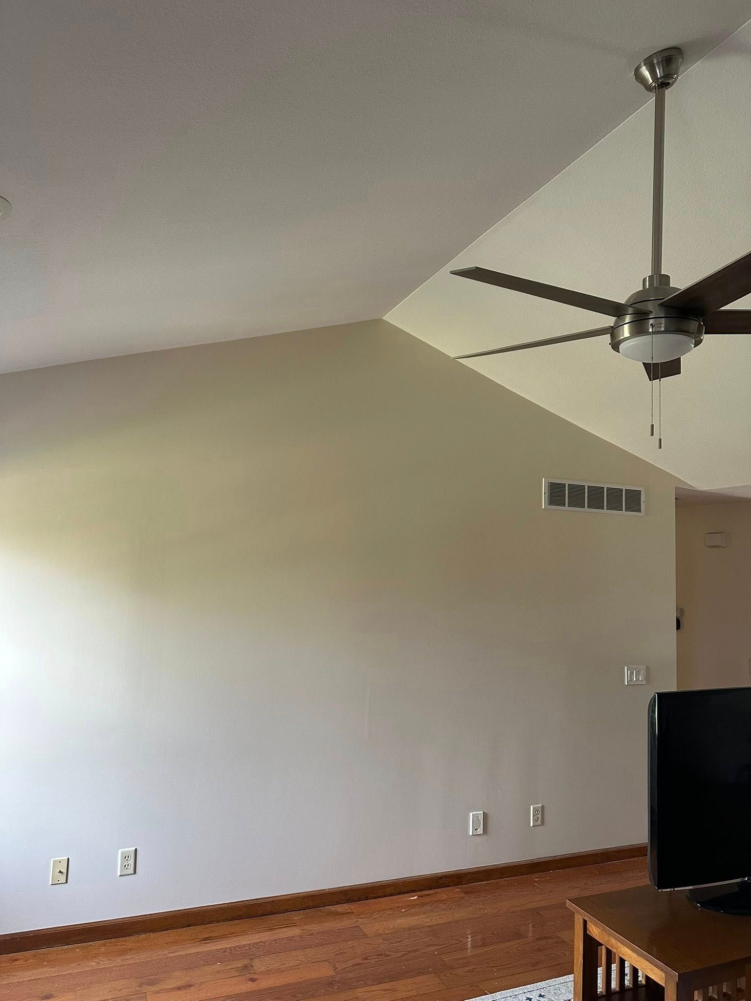 Empty living room with vaulted ceiling, ceiling fan, beige walls, and hardwood floor