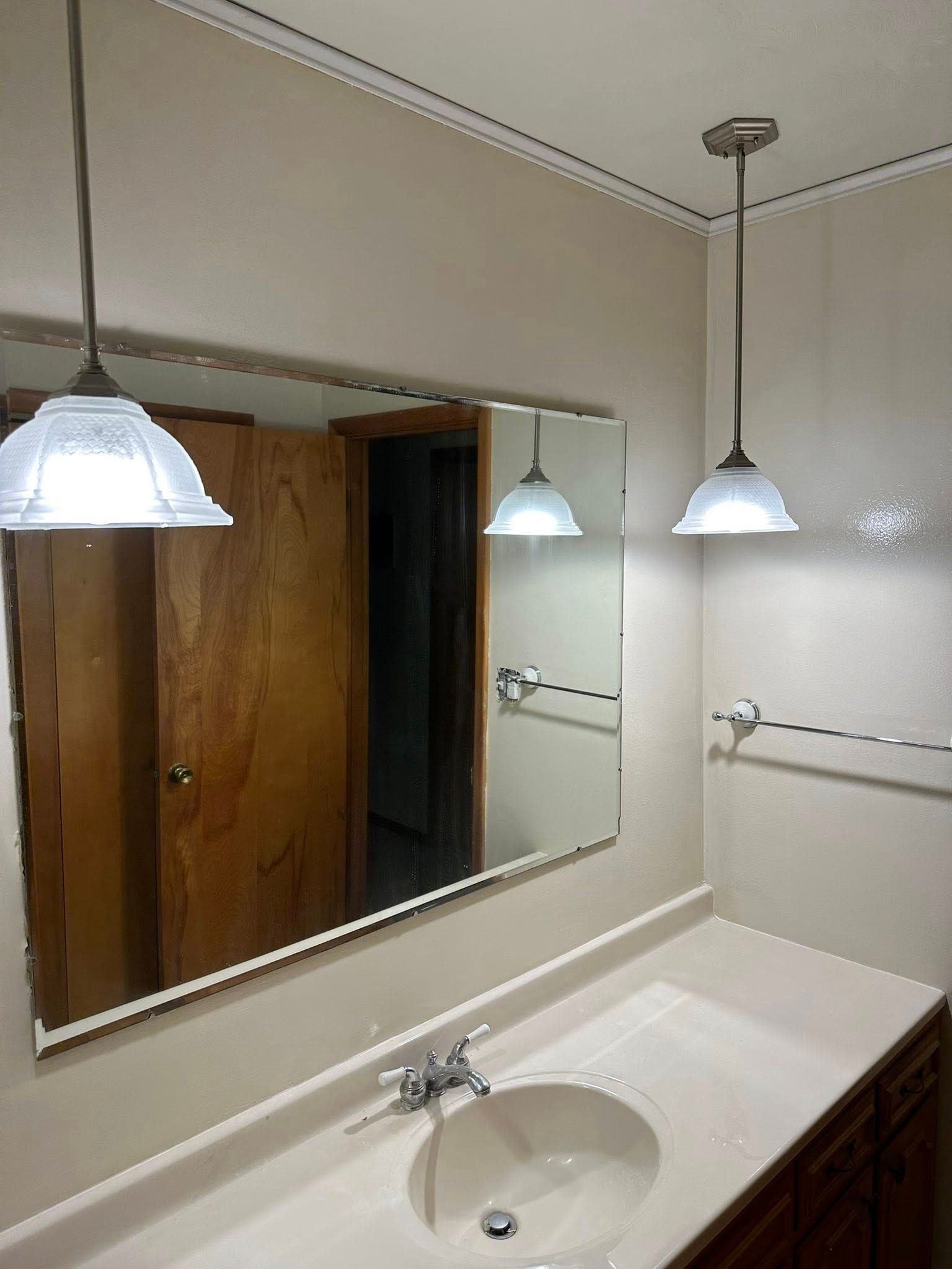 Bathroom vanity with mirror, white sink, and three pendant lights above a dark wood counter.
