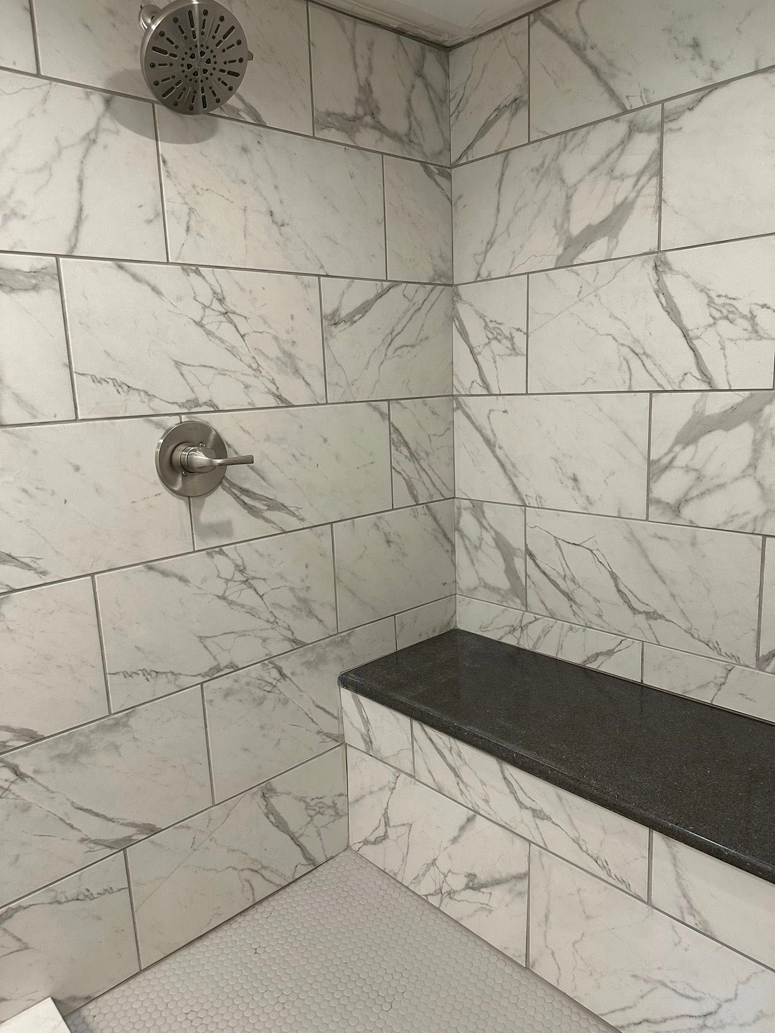 Tiled shower corner with a dark stone bench and chrome shower fixtures