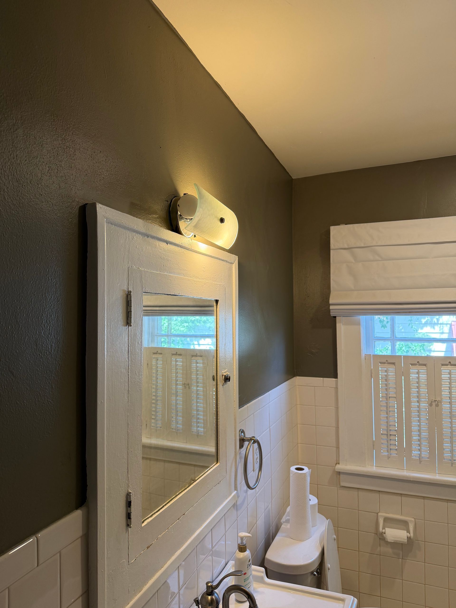 Small bathroom with mirror, light fixture, toilet, window, and white towel-covered items.