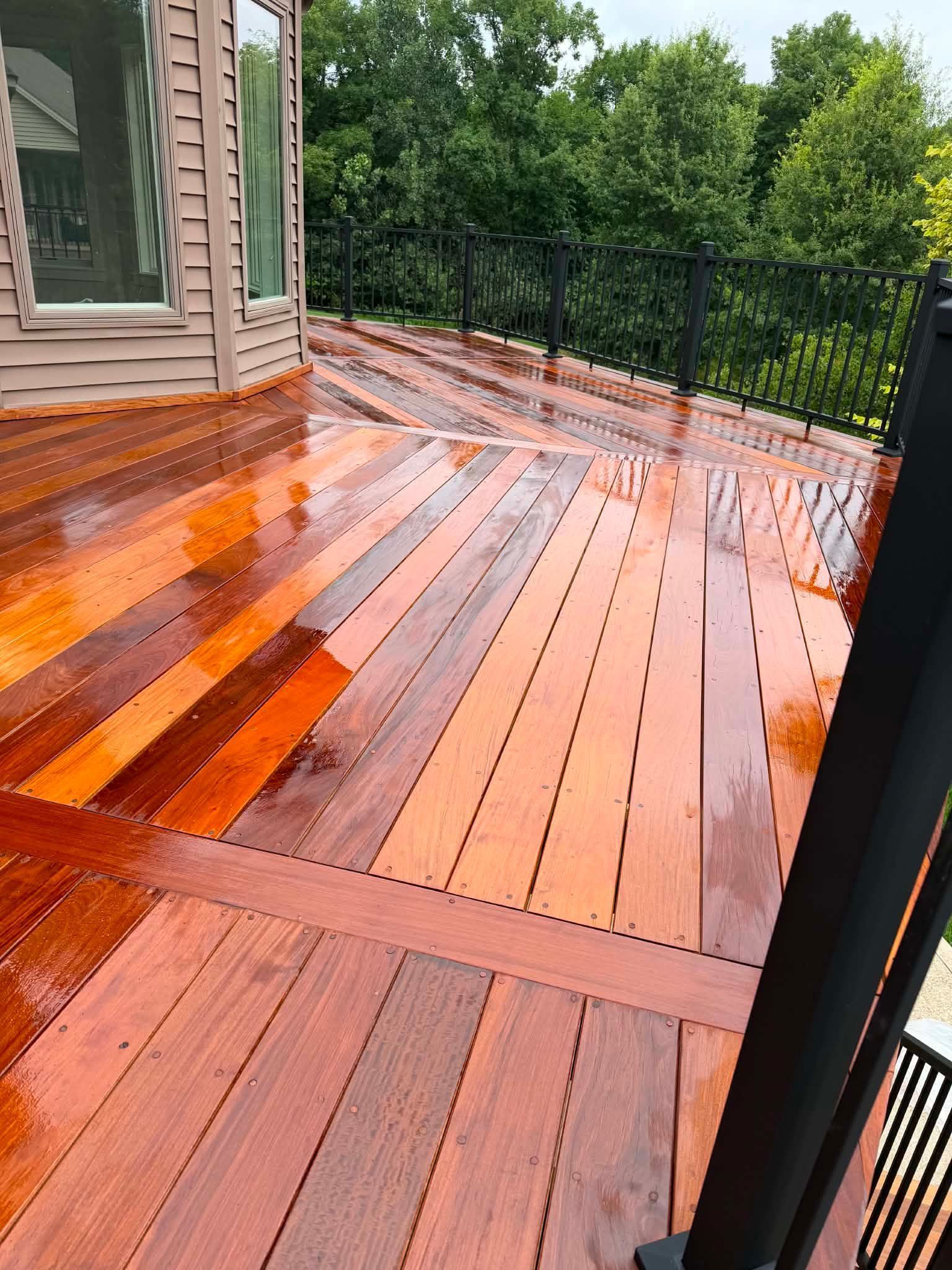 Wet wooden deck beside a house, reflecting rain under a green backyard fence.