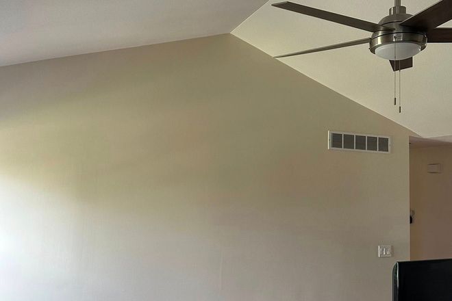 Living room with beige walls, vaulted ceiling, ceiling fan, and wall vent.