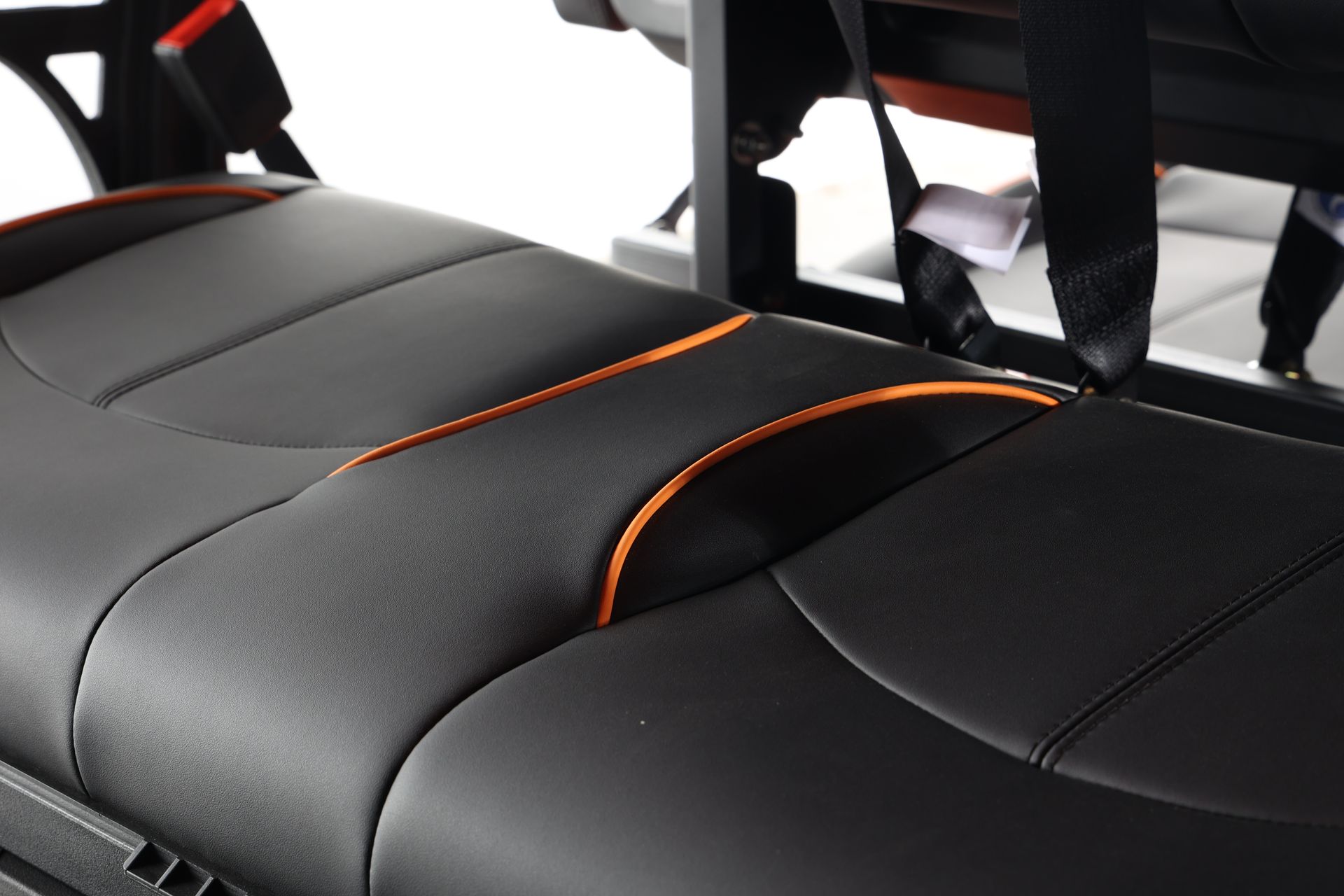A close up of a black leather seat with orange stitching