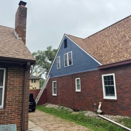 Brick house exterior with blue gable, red brick walls, white-trimmed windows, and a chimney along a narrow side yard