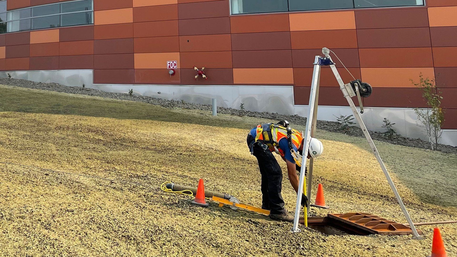 A man is measuring a hole in the ground in front of a building.