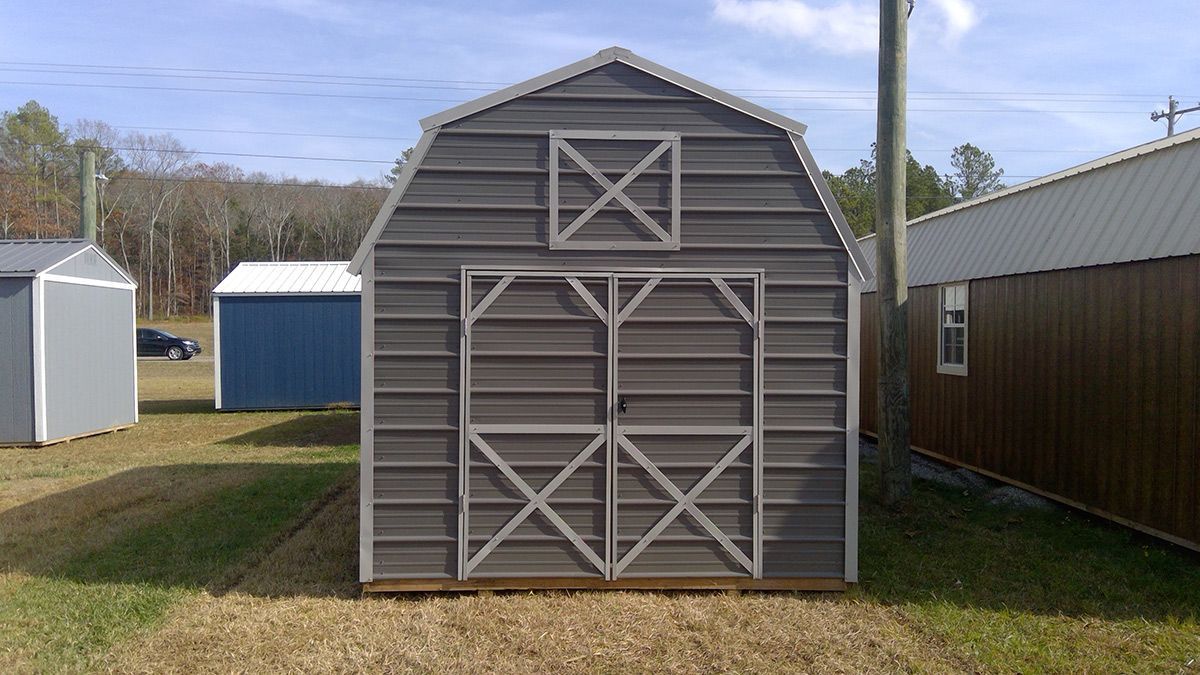A barn shaped shed is sitting in the middle of a grassy field.