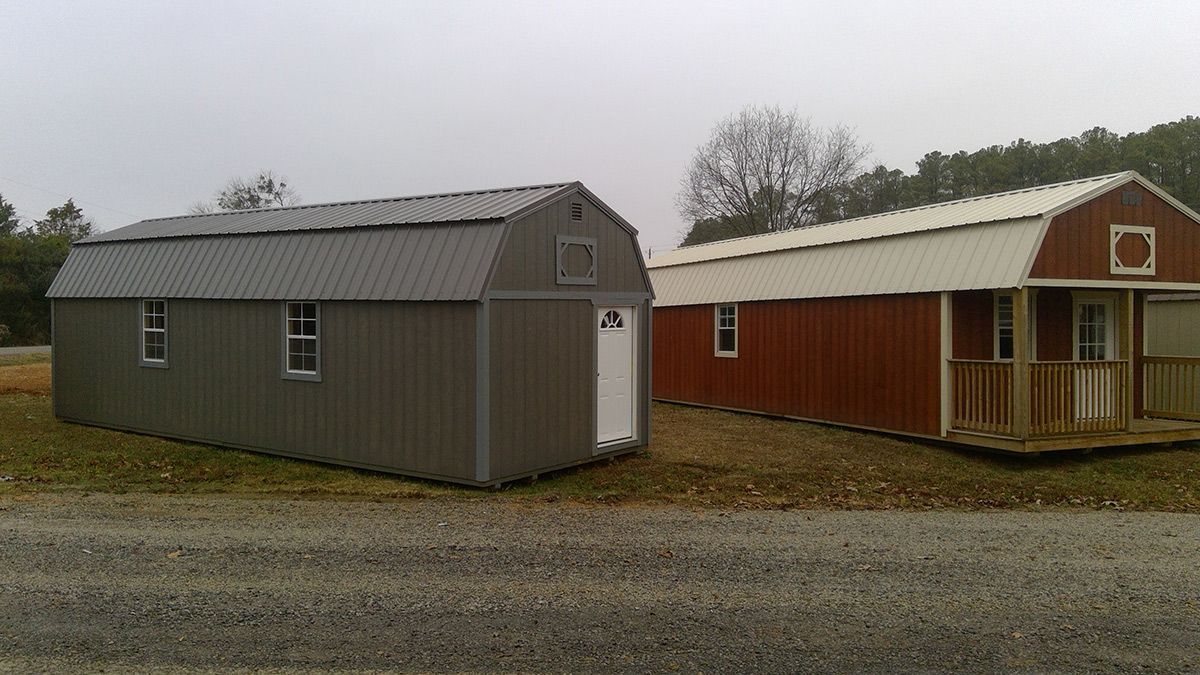 Two sheds are sitting next to each other on a gravel road.