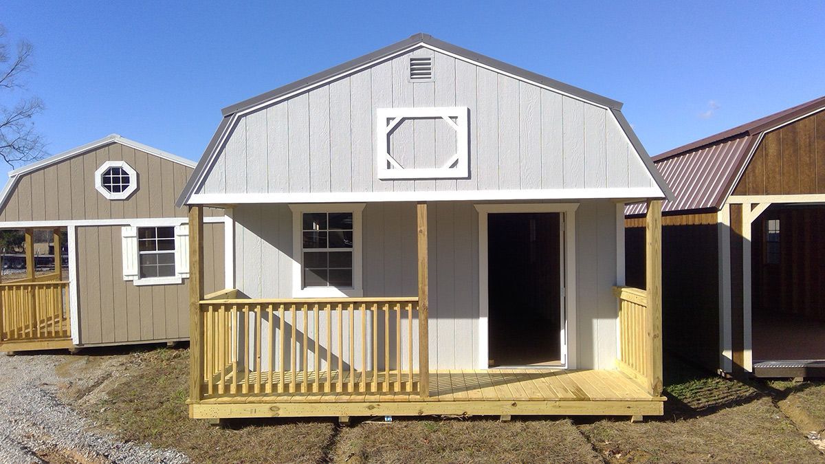 A small house with a porch is sitting on top of a dirt field.
