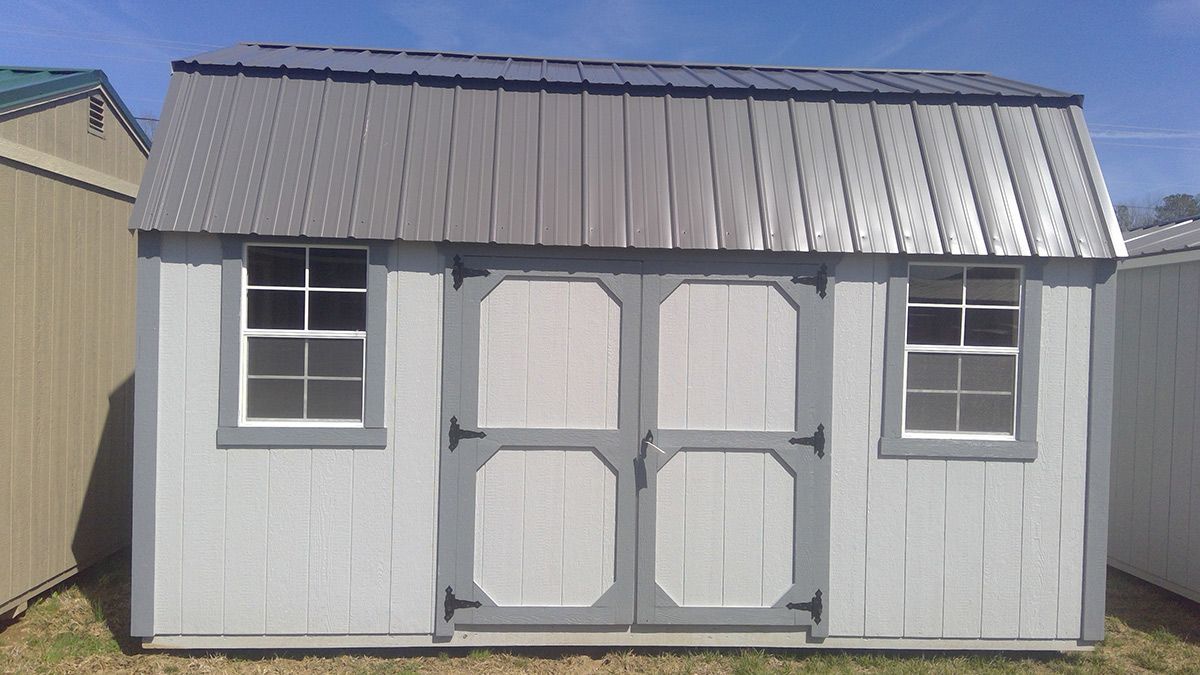 A white shed with a metal roof and windows is sitting in the grass.