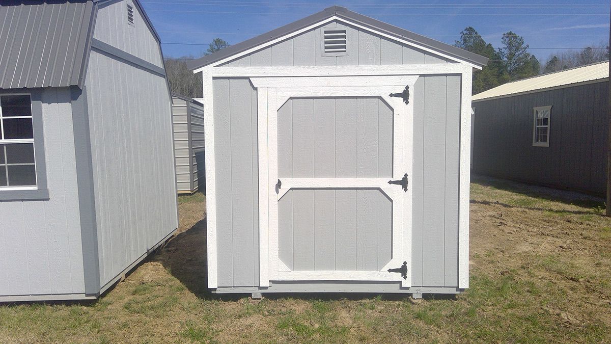 A gray and white shed is sitting in the middle of a grassy field.