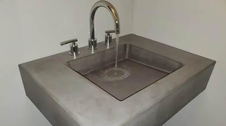 Concrete sink with running faucet and small side spout, water flowing into a square basin