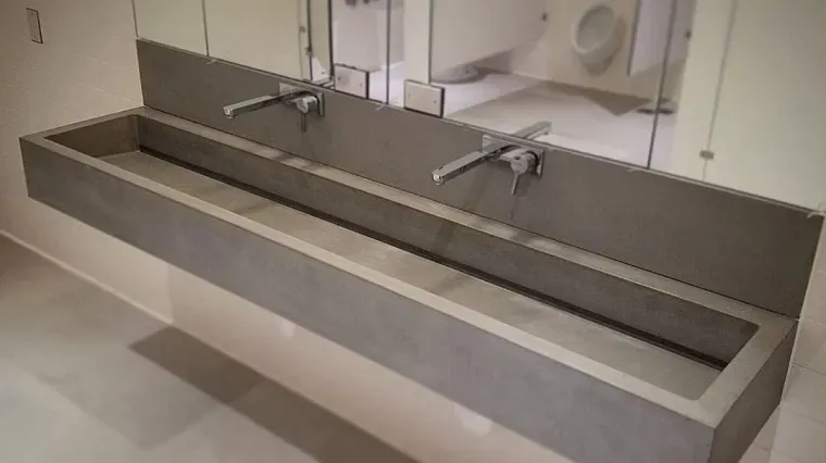 Modern public restroom sink area with two faucets and a long gray countertop