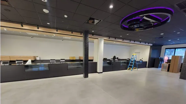 Empty modern lobby with black reception desk, purple ceiling light, and a ladder near the back wall