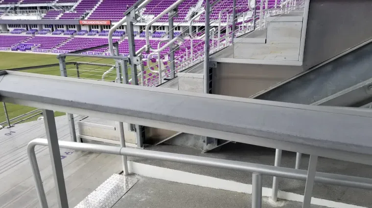 Empty stadium seating with purple seats and metal railings along a concrete concourse.
