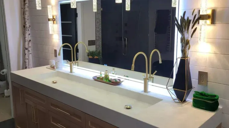 Modern bathroom vanity with double gold faucets, large mirror, and white countertop.