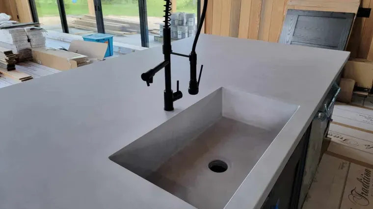 Kitchen island with a black faucet and rectangular sink under construction, near large windows.