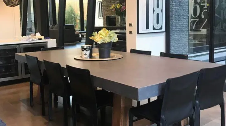 Modern dining table with black chairs and a small flower centerpiece in a bright indoor setting