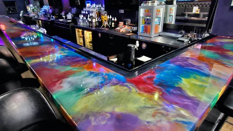 Colorful epoxy bar counter with a glossy rainbow swirl in a dimly lit nightclub setting