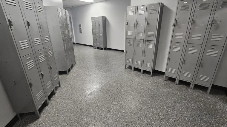 Empty school locker room with gray metal lockers and speckled tile floor