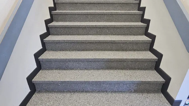 Carpeted indoor staircase with gray steps and black-edged trim between white walls