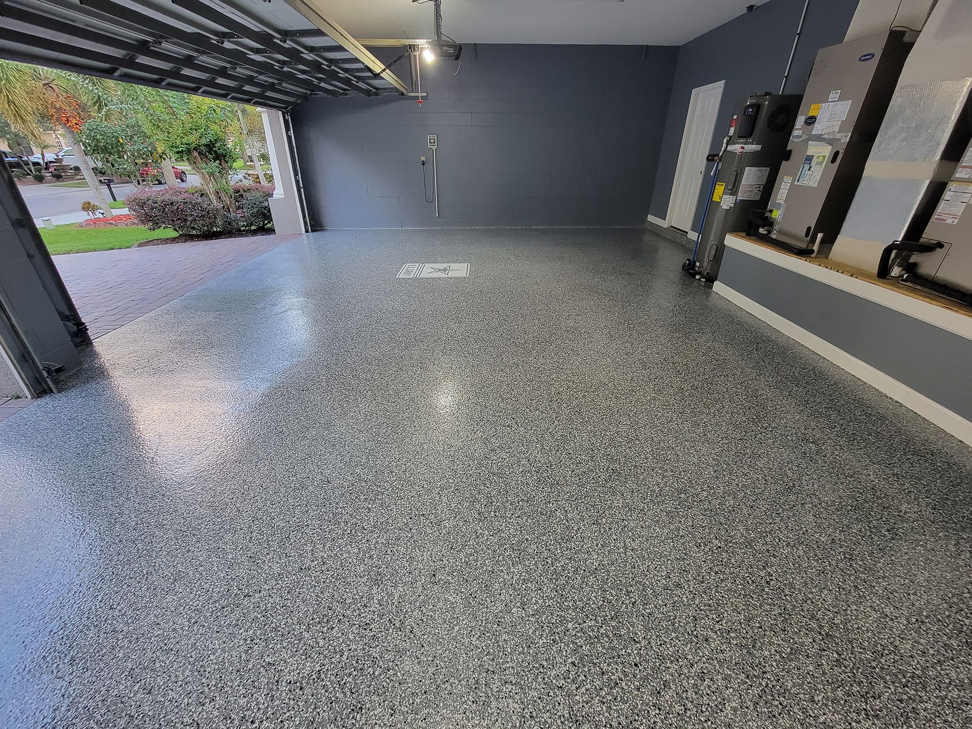 Spacious empty garage with gray epoxy floor, open door to outside, and utility panels on the wall