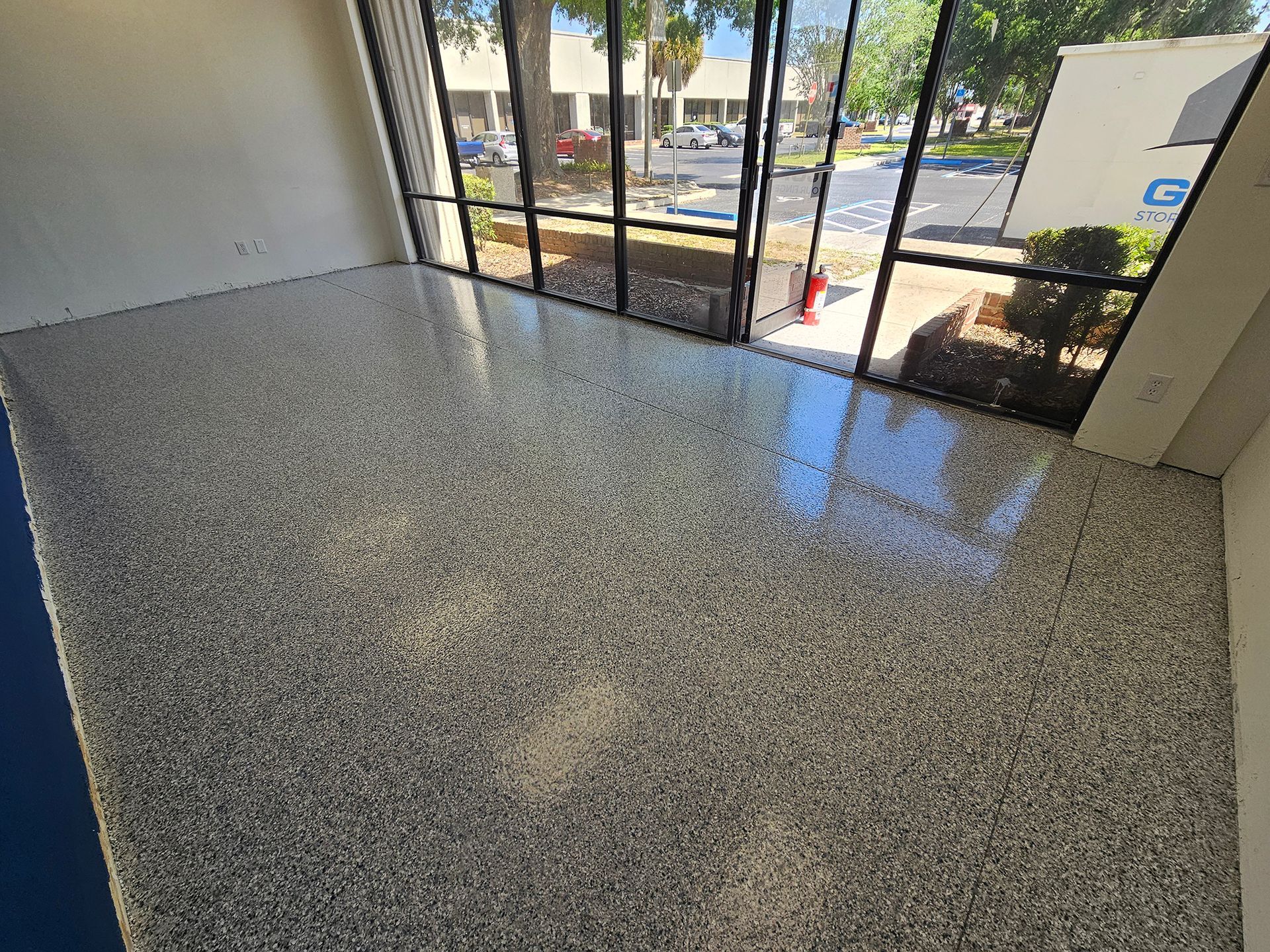 Empty polished speckled floor by a glass storefront entrance, with street view outside.